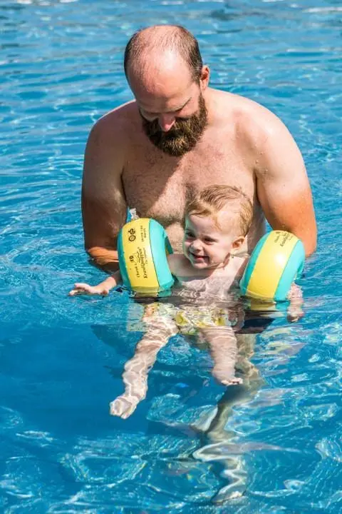 Otec s dieťaťom s rukávnikmi v bazéne