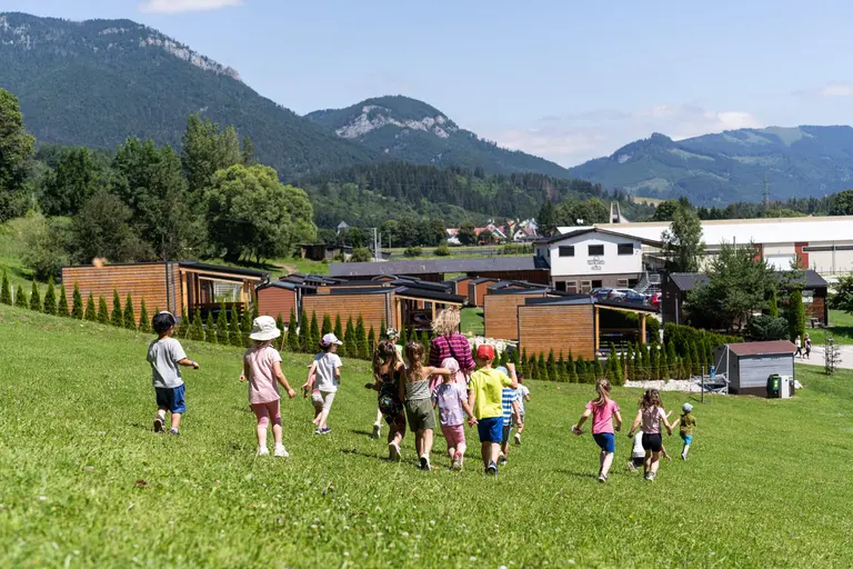 Deti a dospelá osoba kráčajú po tráve pri chatkách vo Villa Betula Resort.