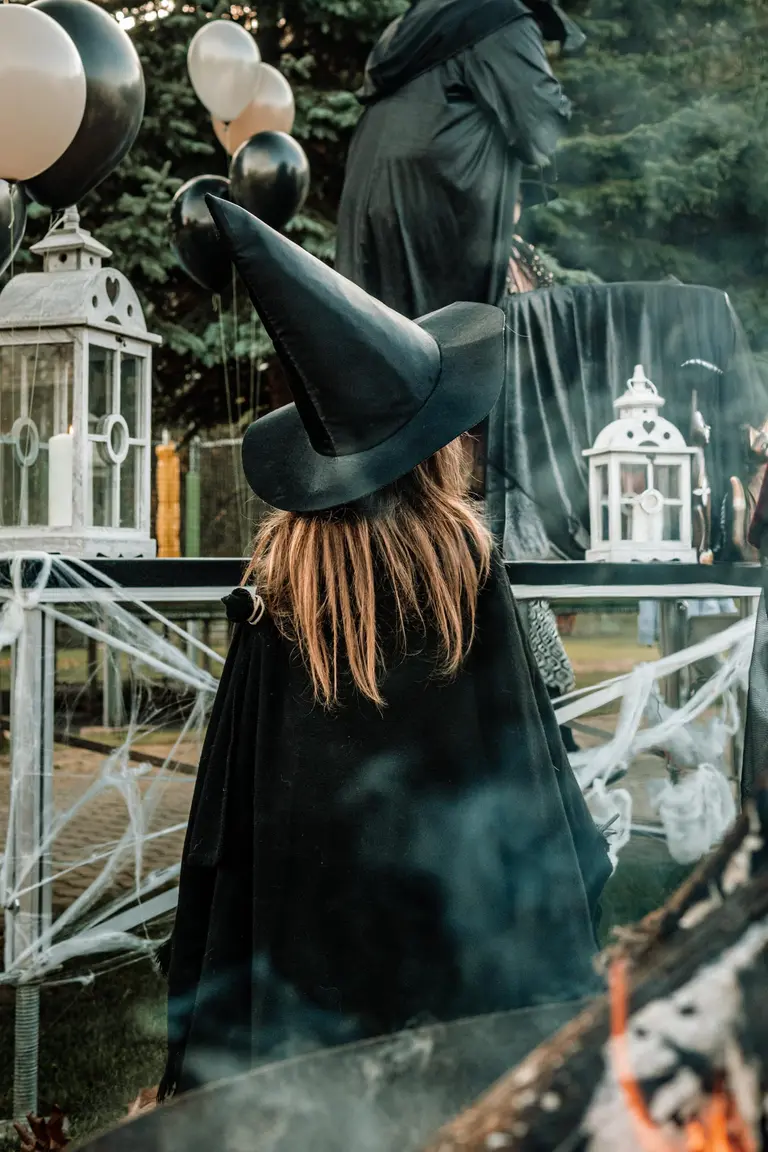 Dievča v čarodejníckom klobúku obklopené halloweenskou výzdobou vo Villa Betula Resort.