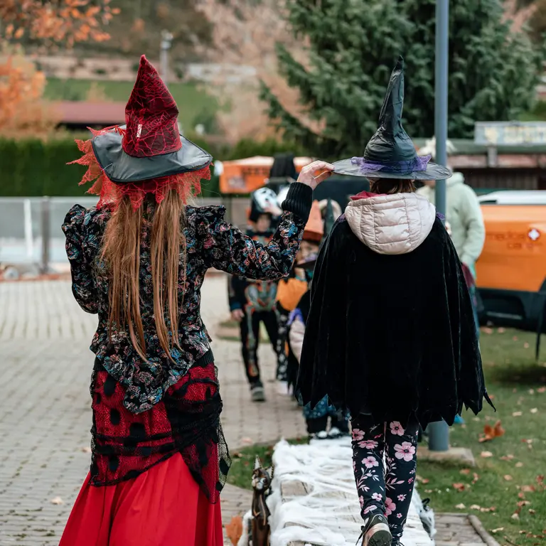 Dve deti v kostýmoch čarodejníc kráčajú na halloweenskom podujatí vo Villa Betula Resort.
