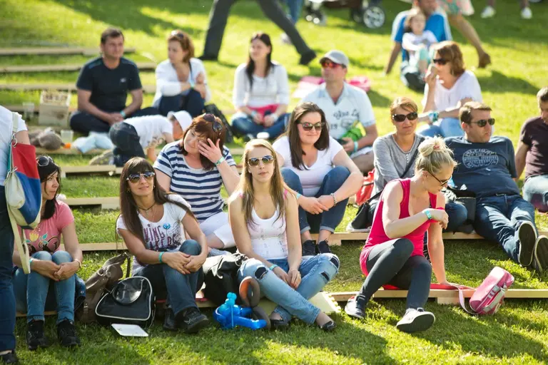 Ľudia sedia na trávniku vo Villa Betula Resort, sledujú Family Days.