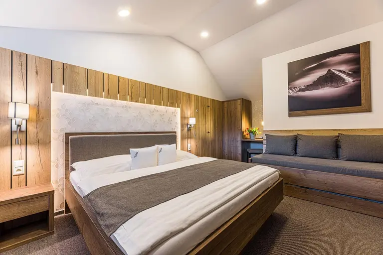 Útulná spálňa s manželskou posteľou, drevenými prvkami a gaučom vo Villa Betula Resort.