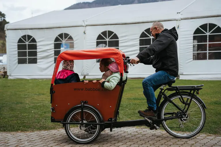 Deti sa vozia v cargo bicykli pri bielom stane vo Villa Betula Resort.